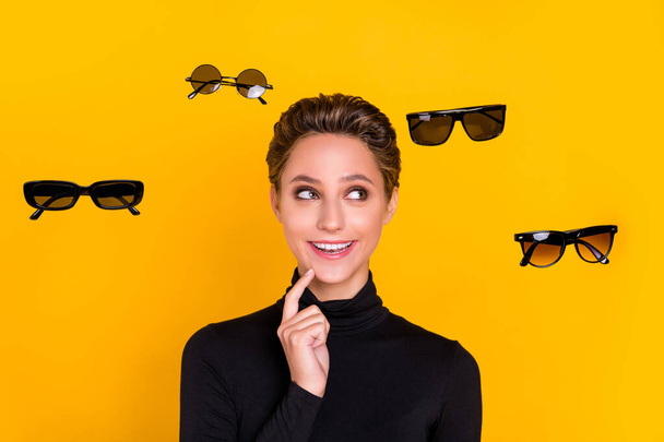 Portrait of attractive minded cheerful girl choosing news specs thinking isolated over bright yellow color background - Foto, afbeelding
