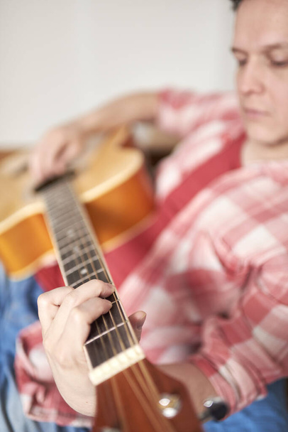 Jeune homme hispanique jouant de la guitare à la maison. Des concepts de musique, de passe-temps et de tranquillité. Focus sélectif dans la main gauche. - Photo, image