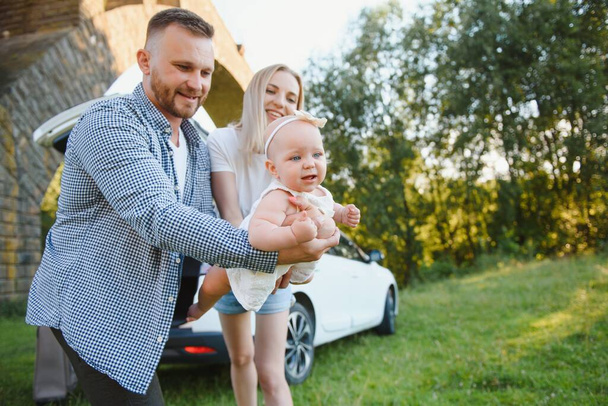 Famiglia giovane tre persone in abiti bianchi hanno pic-nic. Bei genitori e figlia viaggiano in auto durante le vacanze estive. Scena in parco - Foto, immagini