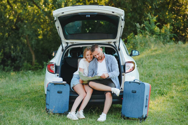 Couple of traveler sitting on hatchback of car near the road during holiday. - Φωτογραφία, εικόνα