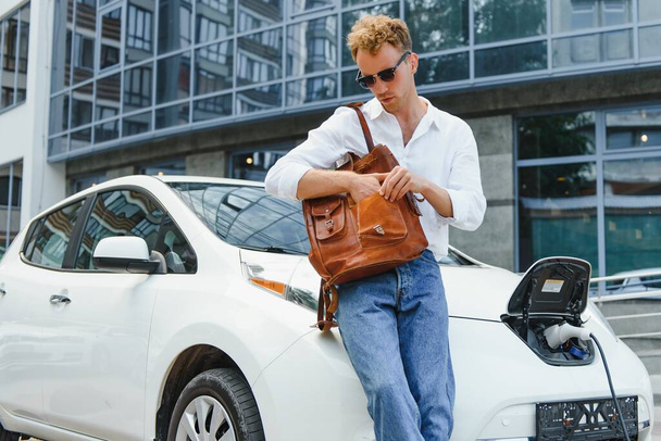A handsome young man is charging his modern electric car. - 写真・画像