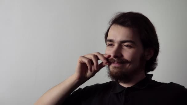 Jeune homme est assis et frisant sa moustache avec un sourire délicat sur son visage - Séquence, vidéo