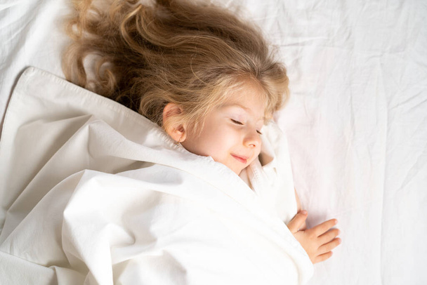 Маленька блондинка солодко спить у ліжку з білою білизною. простір для тексту. здоровий сон дитини
. - Фото, зображення