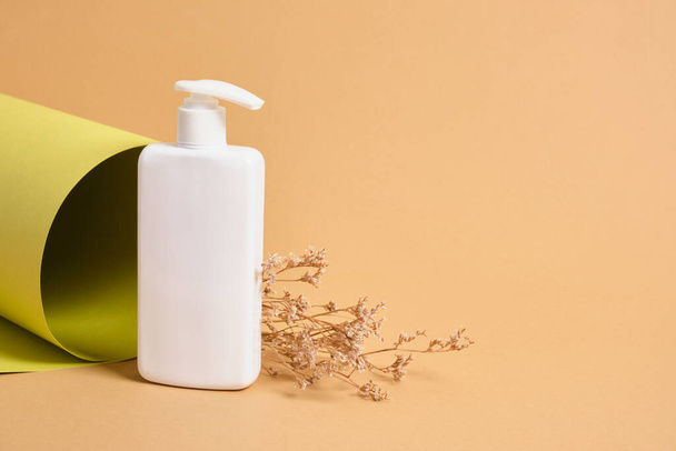 flower and mock up blank white bottle with dispenser for cosmetics on the background of a roll of green paper texture, natural cosmetics concept - 写真・画像