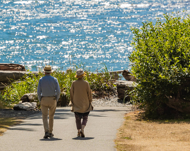 Açık deniz kıyısında bir parkta yürüyen etkin yaşlı bir çiftin güzel manzarası. Boşluğu kopyala, seyahat fotoğrafı, sokak görünümü, seçici odak, bulanık. - Fotoğraf, Görsel