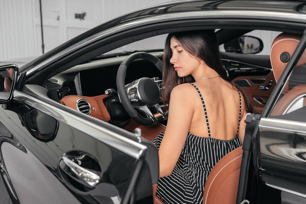 Jovem mulher asiática sentada em carro de luxo na garagem antes de iniciar o motor - Foto, Imagem