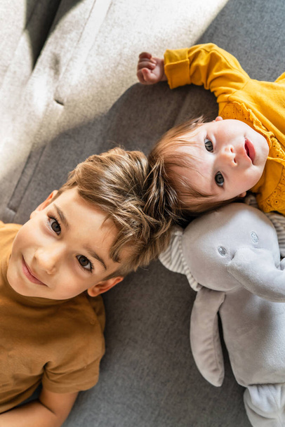 mały biały chłopiec pięć lat leżący na łóżku z jego młodszy brat lub siostra patrząc w aparat z góry w dół widok - Zdjęcie, obraz