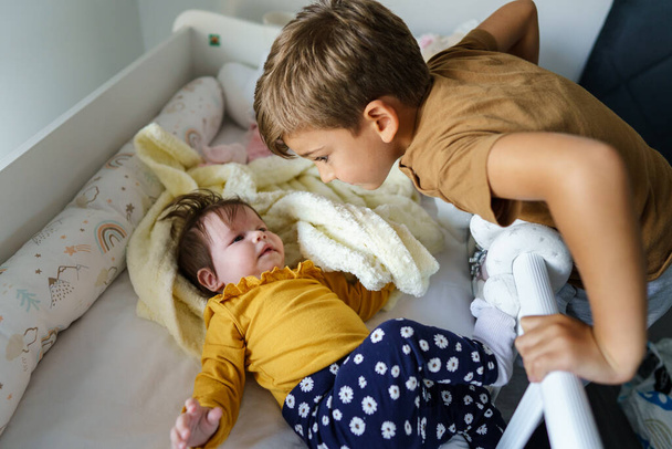 mały biały chłopiec pięć lat bawiąc się z jego młodszy brat lub siostra dbanie w łóżeczko prawdziwe ludzie rodzina więzi rodzeństwo brat i siostra pojęcie - Zdjęcie, obraz