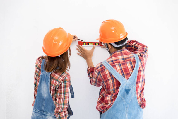 young asian couple in dress plaids shirt and bear cloth working and helping water level measurements on white walls couple teamwork interior decoration renovation modern room concept - Photo, Image