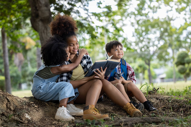 dzieci Afroamerykanie etniczność siedzi do swoich sióstr czytając książkę w parku - Zdjęcie, obraz