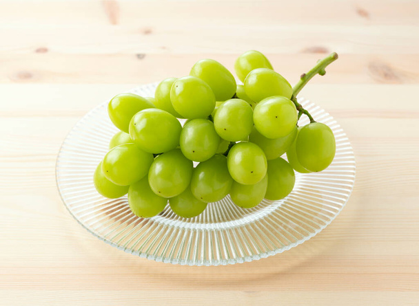 Bunch of Shine-Muscat grapes on a plate set against a wooden background. White grapes. Japanese grapes.  - Photo, Image