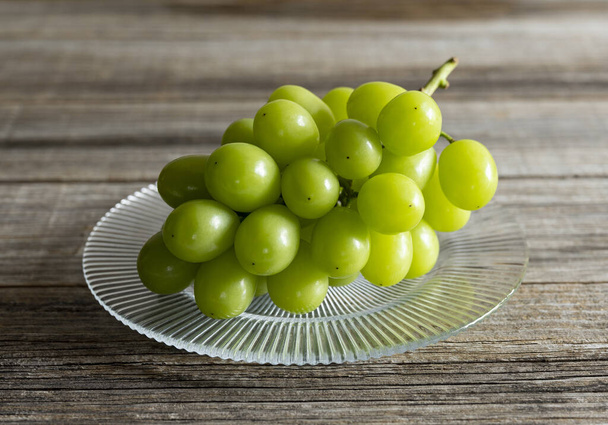 Shine Muscat grapes on a glass plate set against a wooden background. White grapes. Japanese grapes. - Photo, Image
