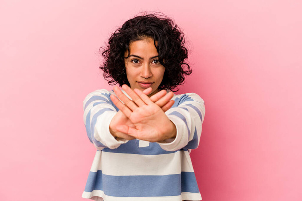 Joven mujer latina rizada aislada sobre fondo rosa haciendo un gesto de negación - Foto, imagen