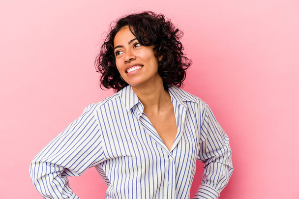 Young curly latin woman isolated on pink background confident keeping hands on hips. - Photo, Image
