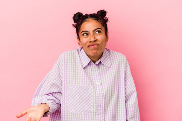 Young latin woman isolated on pink background shrugs shoulders and open eyes confused. - Photo, Image