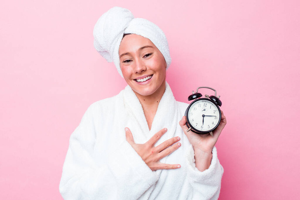 Young australian woman leaving the shower late isolated on pink background laughs out loudly keeping hand on chest. - Fotografie, Obrázek