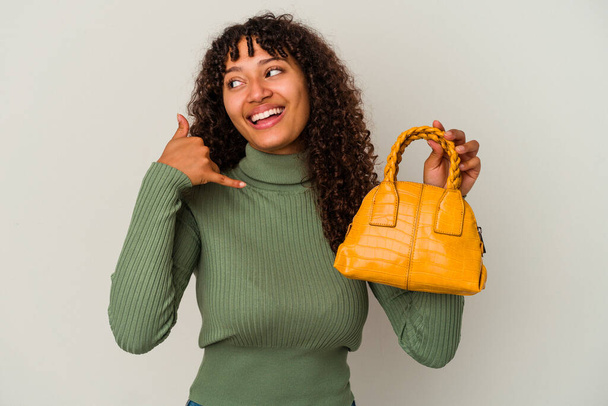Young mixed race woman holding a handbag isolated on white background showing a mobile phone call gesture with fingers. - Foto, immagini