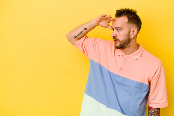 Young tattooed caucasian man isolated on yellow background looking far away keeping hand on forehead. - Photo, Image