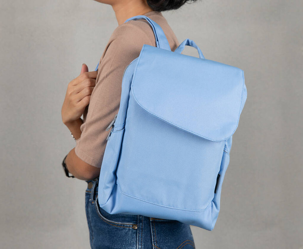 Isolated close up studio shot of female model in brown long sleeve shirt and jeans stand hanging blue multipurpose bag on shoulder on white background. - Zdjęcie, obraz
