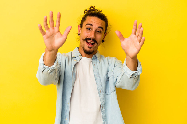 Young caucasian man with long hair isolated on yellow background celebrating a victory or success, he is surprised and shocked. - Foto, immagini