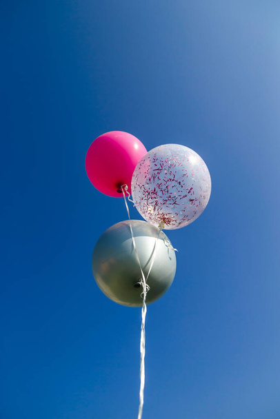 Τρία πολύχρωμα μπαλόνια ηλίου γενεθλίων αιωρούνται στον ουρανό. Κάθετο πλαίσιο με χώρο αντιγραφής στην κορυφή. - Φωτογραφία, εικόνα
