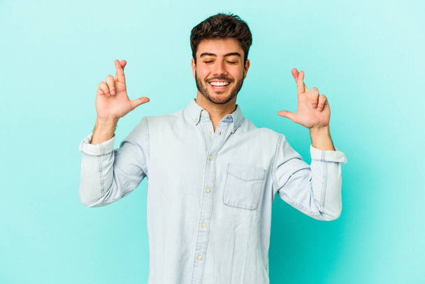Молодий білий чоловік ізольований на синьому фоні, перетинаючи пальці, щоб мати удачу
 - Фото, зображення