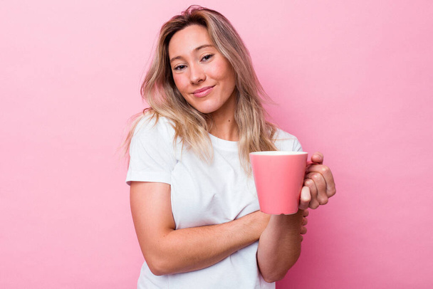 Young australian woman holding a pink mug isolated on pink background laughing and having fun. - Foto, immagini