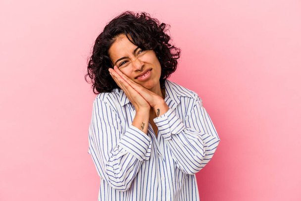 Joven mujer latina rizada aislada sobre fondo rosa bostezando mostrando un gesto cansado cubriendo la boca con la mano. - Foto, imagen
