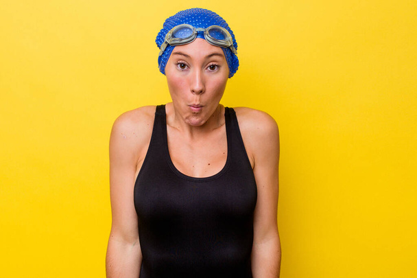 若いオーストラリアの水泳の女性は黄色の背景shrugs肩と開いて目が混乱に孤立. - 写真・画像