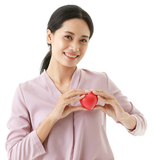 Portret zbliżenie izolowane wyciąć strzał Azji młody szczęśliwy szpital dawca krwi pacjent trzymać czerwone gumowe serce w dłoniach na klatce piersiowej w przednim białym tle z miejsca na reklamę ubezpieczenia. - Zdjęcie, obraz