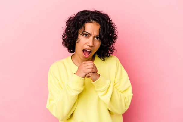 Young curly latin woman isolated on pink background praying for luck, amazed and opening mouth looking to front. - Foto, Bild