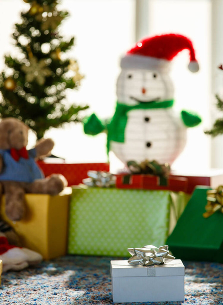 Букет із загорнутих подарунків, розміщених на підлозі біля ялинки та сніговика під час святкування свята вдома
 - Фото, зображення