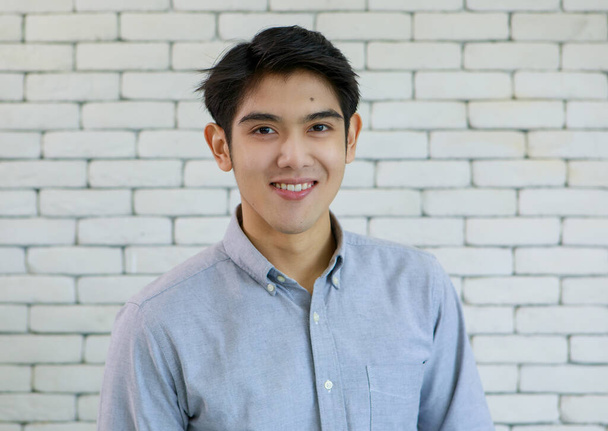 Retrato de joven y guapo hombre asiático con sonrisa y cara amistosa feliz sobre fondo de pared de ladrillo blanco. - Foto, imagen