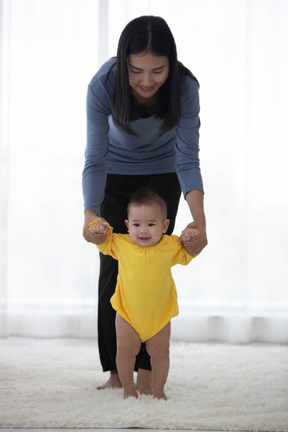 Pystysuoran aasialaisen äidin muotokuva on johtava käsi, jossa lapsi kävelee molemmat hymyillen ja näyttää tyytyväiseltä katsomaan kameraa kirkkaalla valolla aamulla on tausta.. - Valokuva, kuva