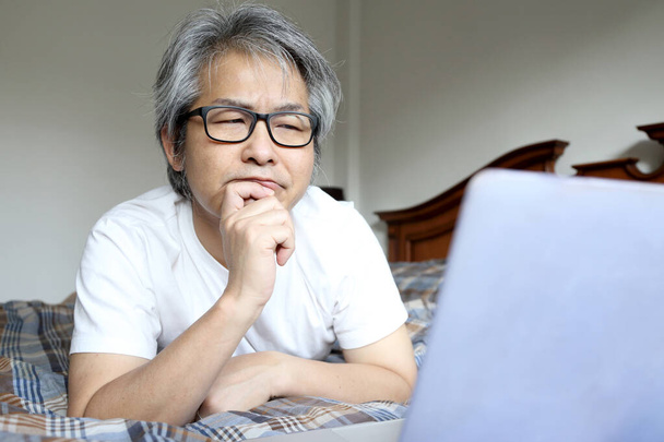 Der asiatische Mann mit Laptop auf dem Bett. - Foto, Bild