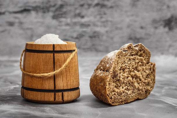 Cut loaf of rye bread with a wooden salt cellar on the gray kitchen table. - Photo, Image