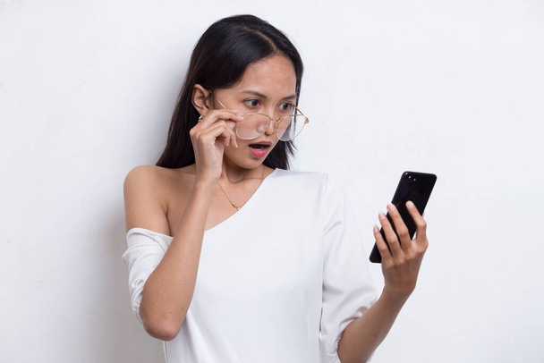 шок молодой азиатской красивой женщины с помощью мобильного телефона изолированы на белом фоне - Фото, изображение
