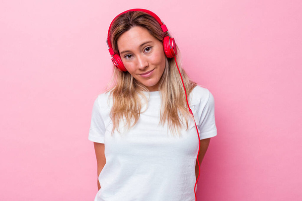 Молода жінка, що слухає музику ізольовану на рожевому фоні, щаслива, усміхнена і весела.. - Фото, зображення