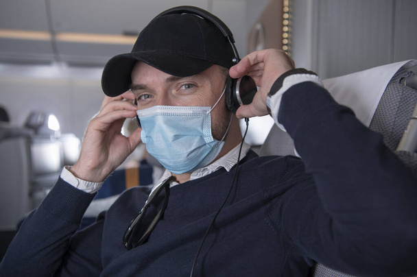 Happy Caucasian Business Class Pasażer w wieku 40 lat w masce ze słuchawkami Słuchać muzyki i oglądać filmy na pokładzie samolotu. - Zdjęcie, obraz