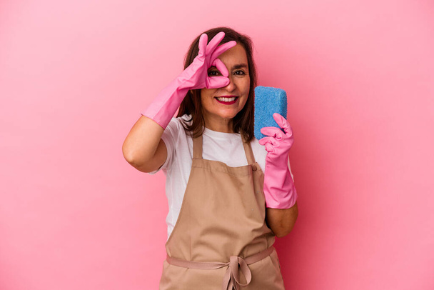 Middle age caucasian woman cleaning home isolated on pink background excited keeping ok gesture on eye. - Фото, зображення