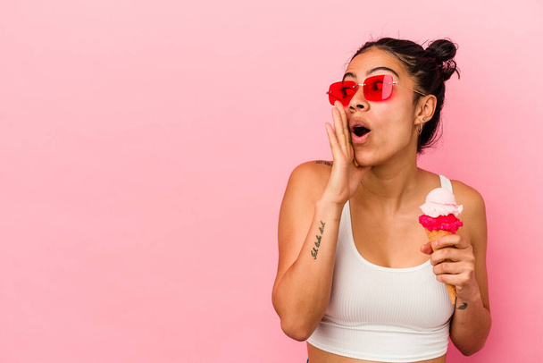 Mladá latinská žena drží zmrzlinu izolované na růžovém pozadí říká tajné horké brzdící zprávy a dívá se stranou - Fotografie, Obrázek