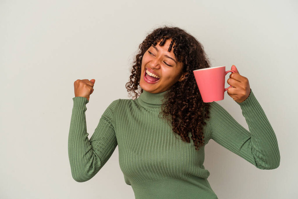 Young mixed race woman holding a mug isolated on white background raising fist after a victory, winner concept. - Photo, Image