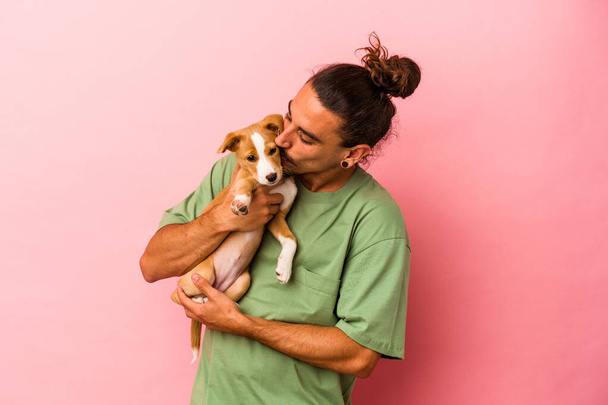 Young caucasian man holding his puppy isolated on pink background - Foto, afbeelding