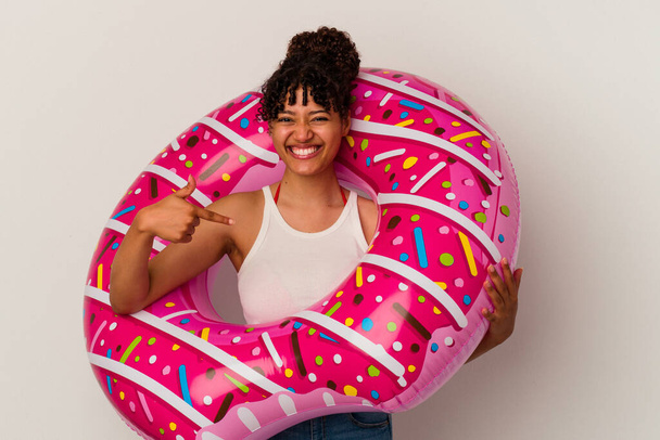 Young mixed race woman holding an inflatable air donut isolated on white background person pointing by hand to a shirt copy space, proud and confident - Φωτογραφία, εικόνα