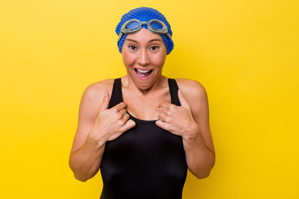 黄色の背景に孤立した若いオーストラリアの水泳の女性は、指で指して驚いて、大きく笑って. - 写真・画像