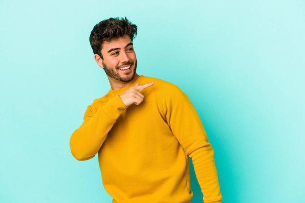 Young caucasian man isolated on blue background looks aside smiling, cheerful and pleasant. - Fotografie, Obrázek