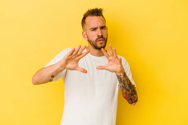 Young tattooed caucasian man isolated on yellow background rejecting someone showing a gesture of disgust. - Photo, Image