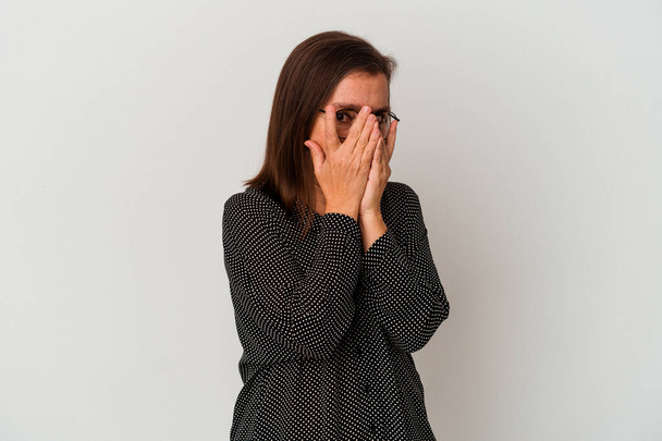 Middle age caucasian woman isolated on white background blink at the camera through fingers, embarrassed covering face. - Photo, Image