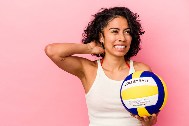 Giovane donna latina che tiene una pallavolo isolata su sfondo rosa che tocca la nuca, pensando e facendo una scelta. - Foto, immagini