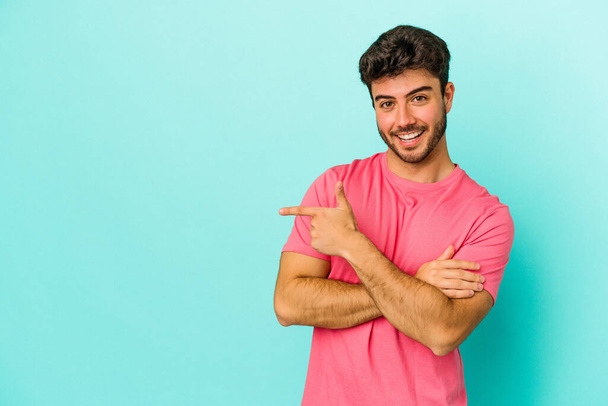 Young caucasian man isolated on blue background smiling cheerfully pointing with forefinger away. - Photo, Image